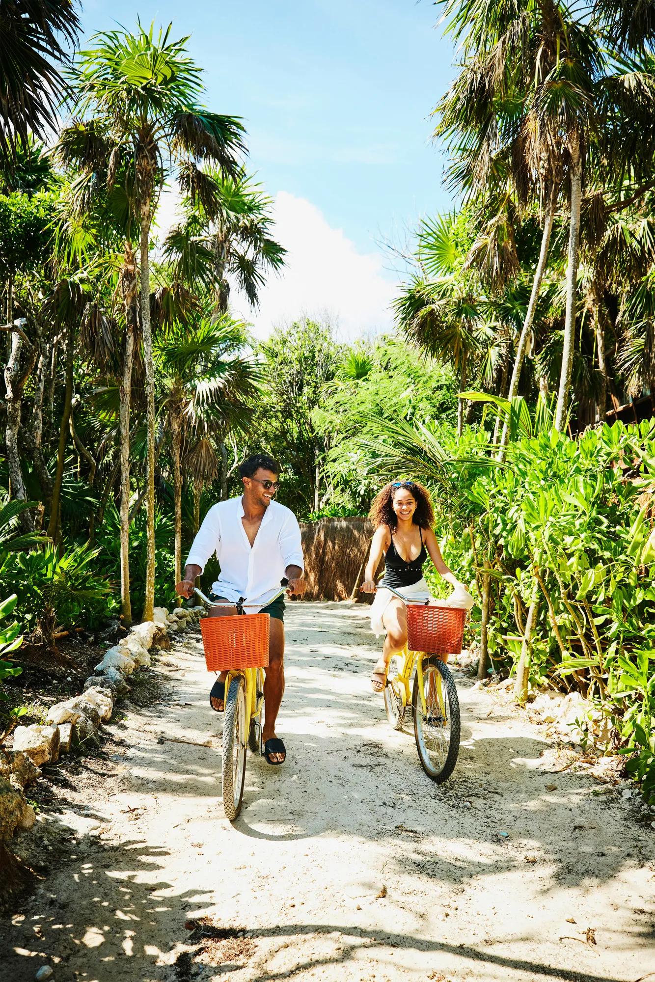 Couple riding bikes down sandy path to the beach in Cancun.