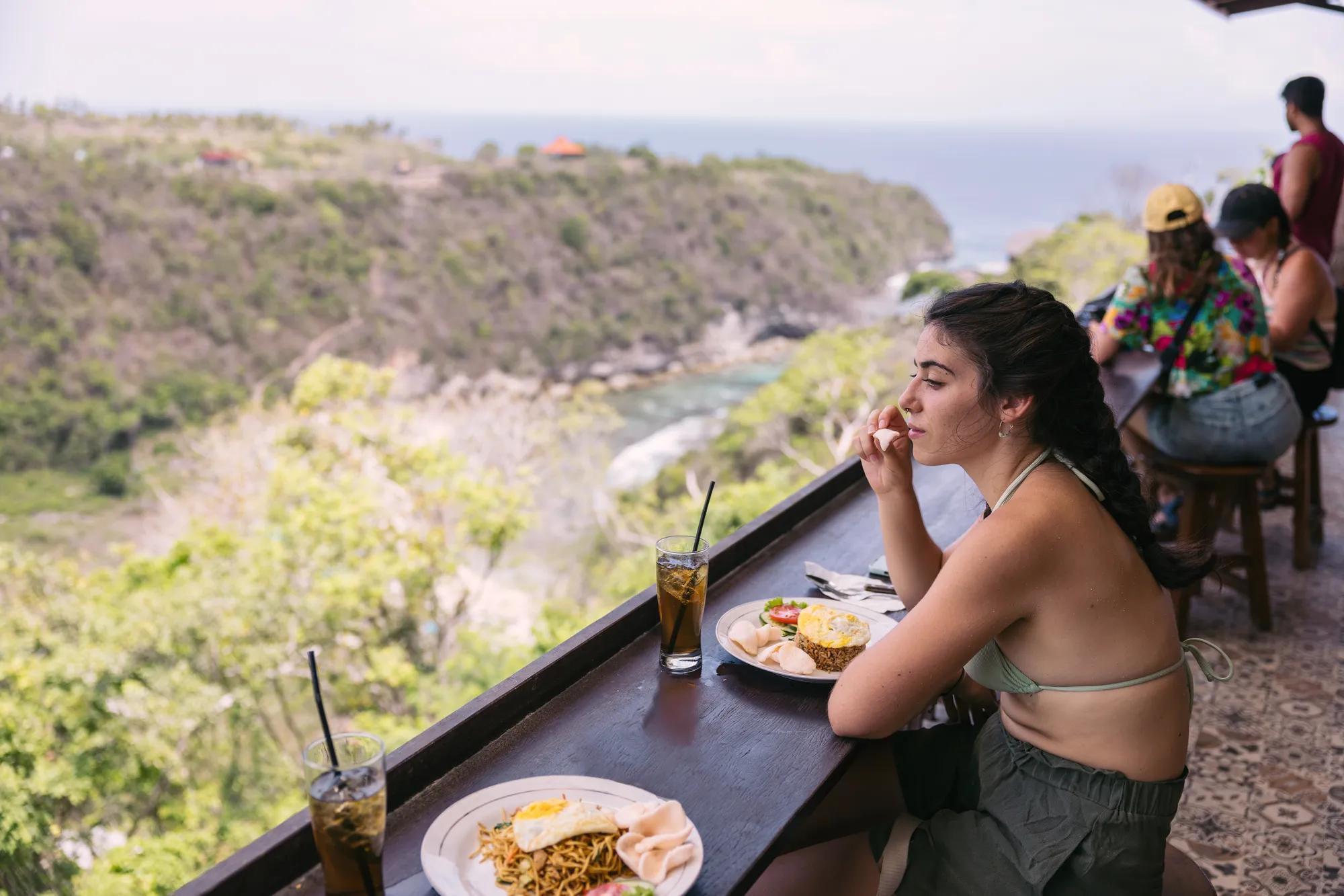 Tourist woman eating nasi goreng, typical balinese food in an open restaurant with beautiful views to the nature